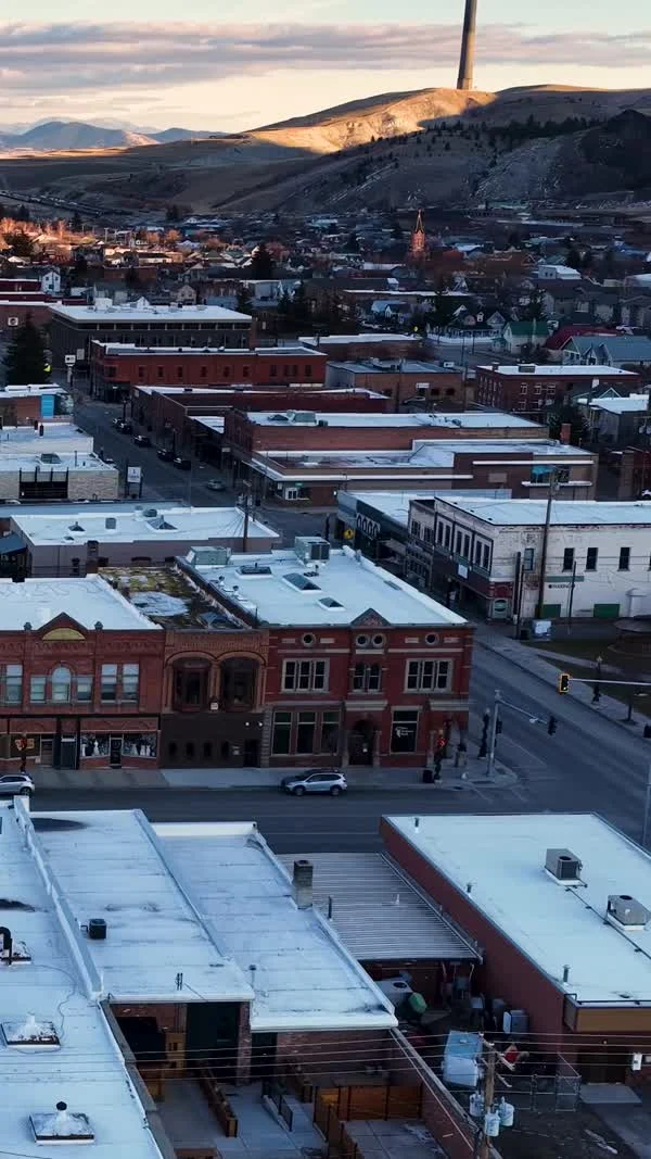 Snow lines the roofs of downtown Anaconda buildings with the stack visible on a hill beyond.