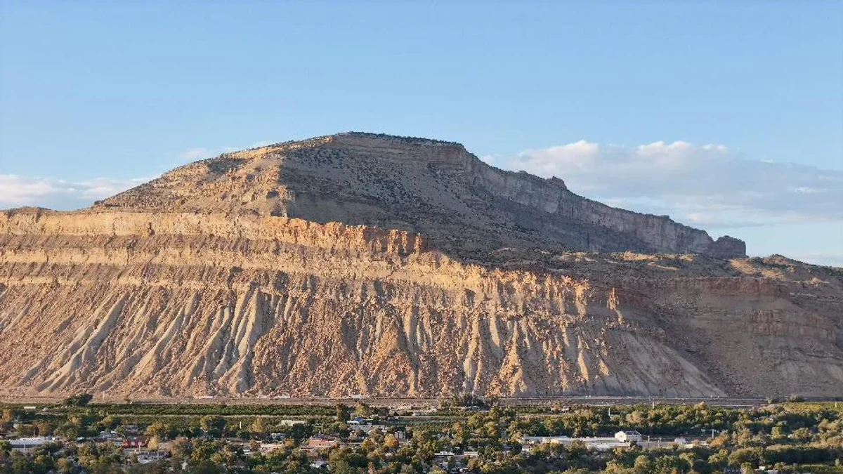 River bend, homes and cultivated rows beneath layered cliffs near Palisade