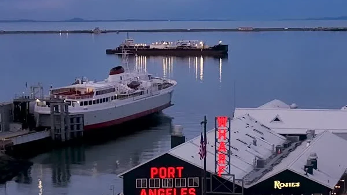 A ferry sits on calm water behind a building with a red Port Angeles sign.