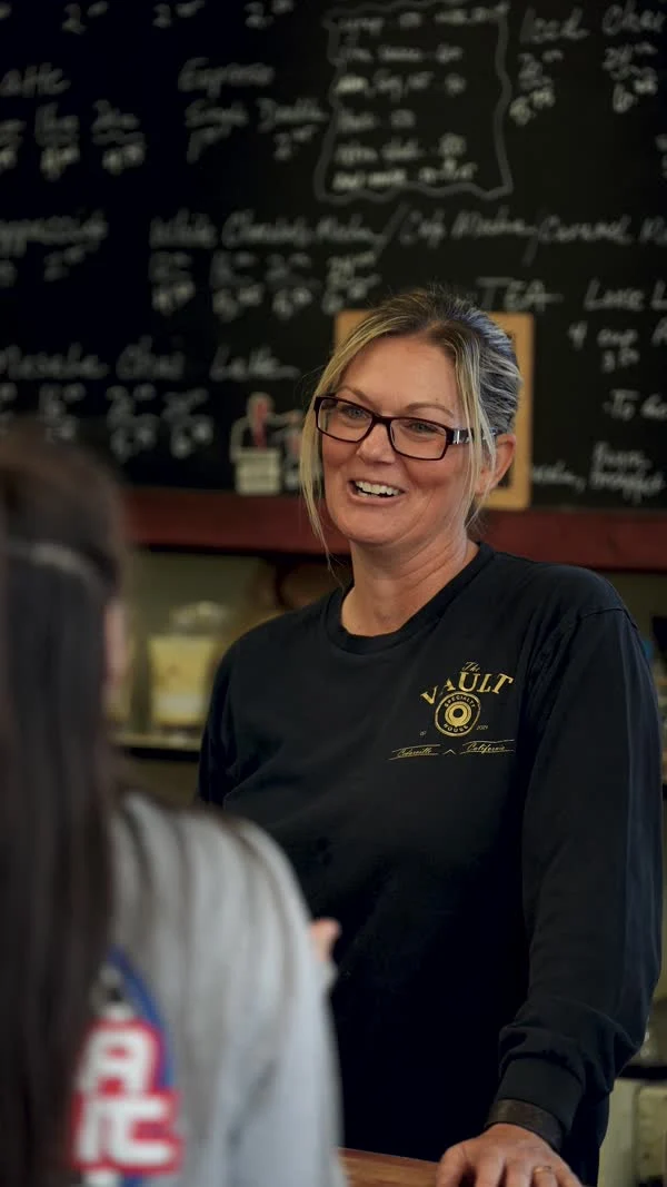 A smiling participant wearing glasses stands behind a counter with a handwritten menu behind her.