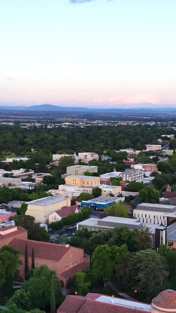 An aerial view looks across leafy Chico streets and downtown buildings at dusk.