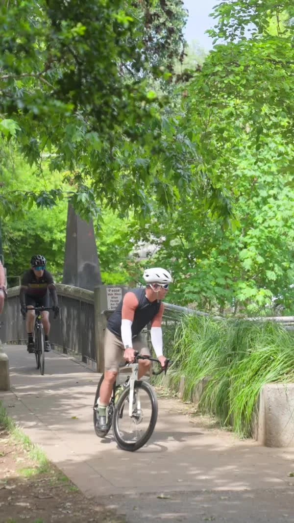 A cyclist rides along a shaded path beside a railing.