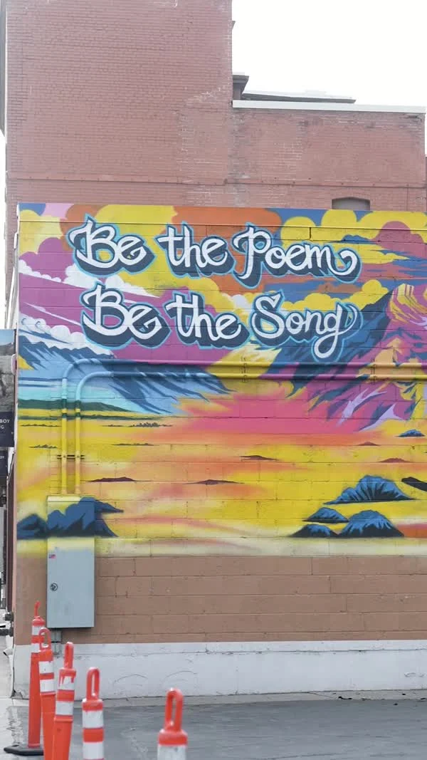 A colorful wall mural reads “Be the Poem / Be the Song.”