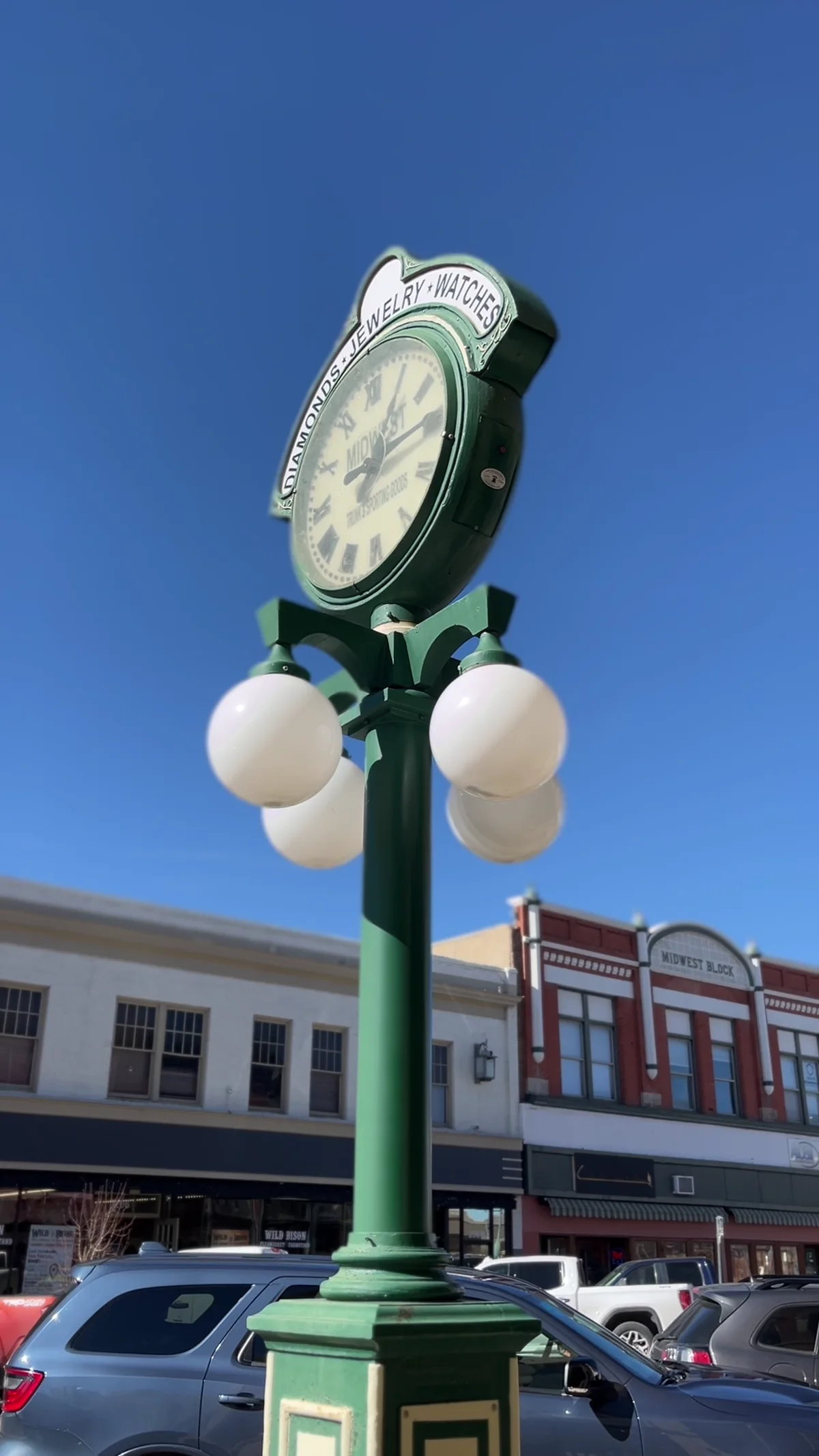 A green jewelry-store street clock stands in front of downtown Laramie storefronts.