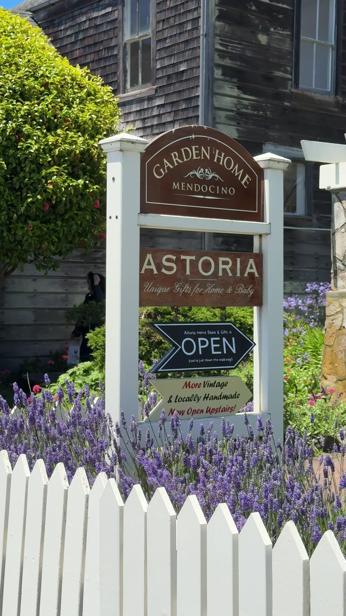 Garden Home Mendocino and Astoria signs behind a white picket fence and flowers.