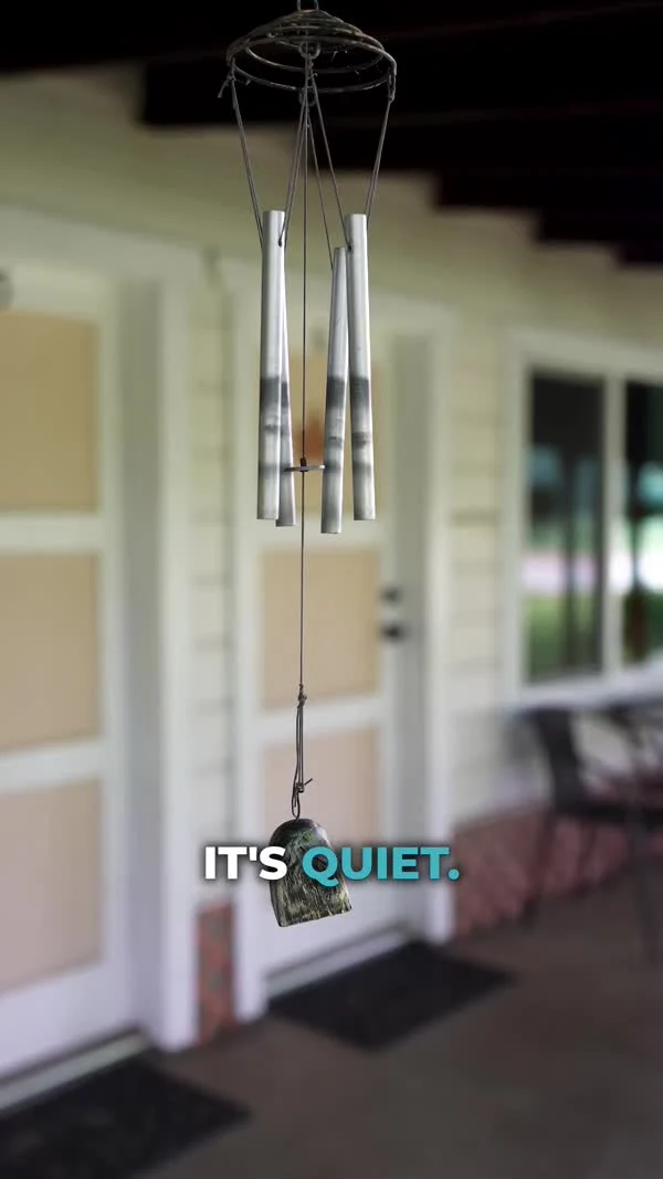 A wind chime hangs in front of a quiet porch with white-framed doors.