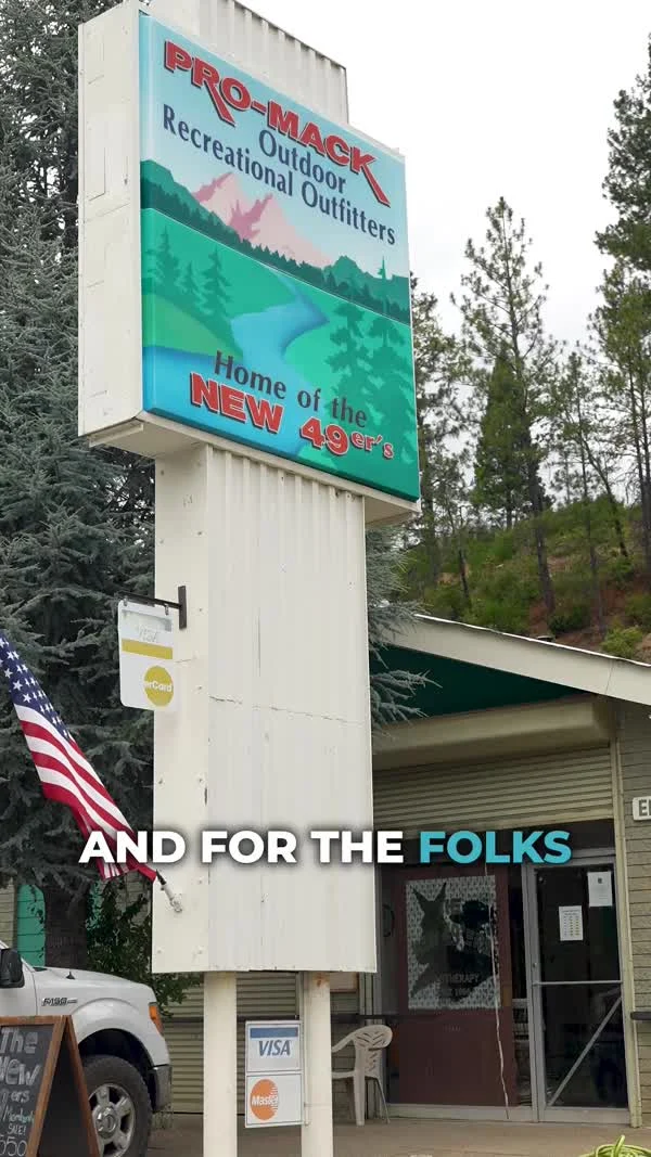 A Pro-Mack Outdoor Recreational Outfitters sign stands beside a small storefront.
