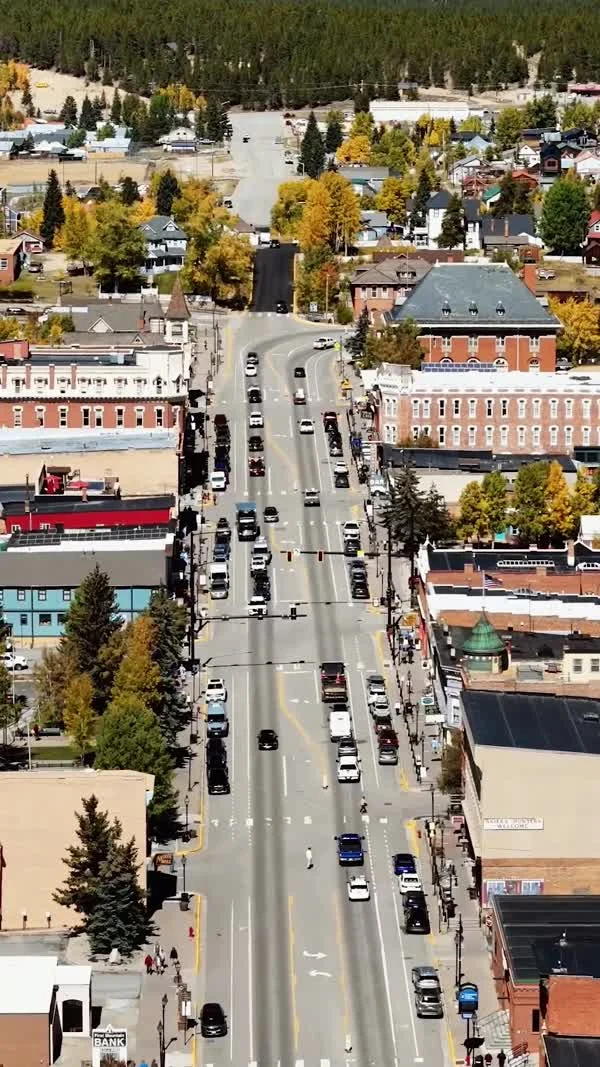 An aerial view follows Leadville’s main street past historic blocks toward autumn trees.