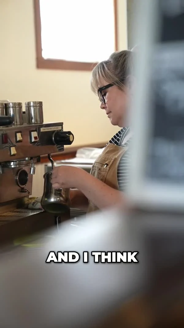 A person wearing an apron works at an espresso machine in a McCloud coffee shop.