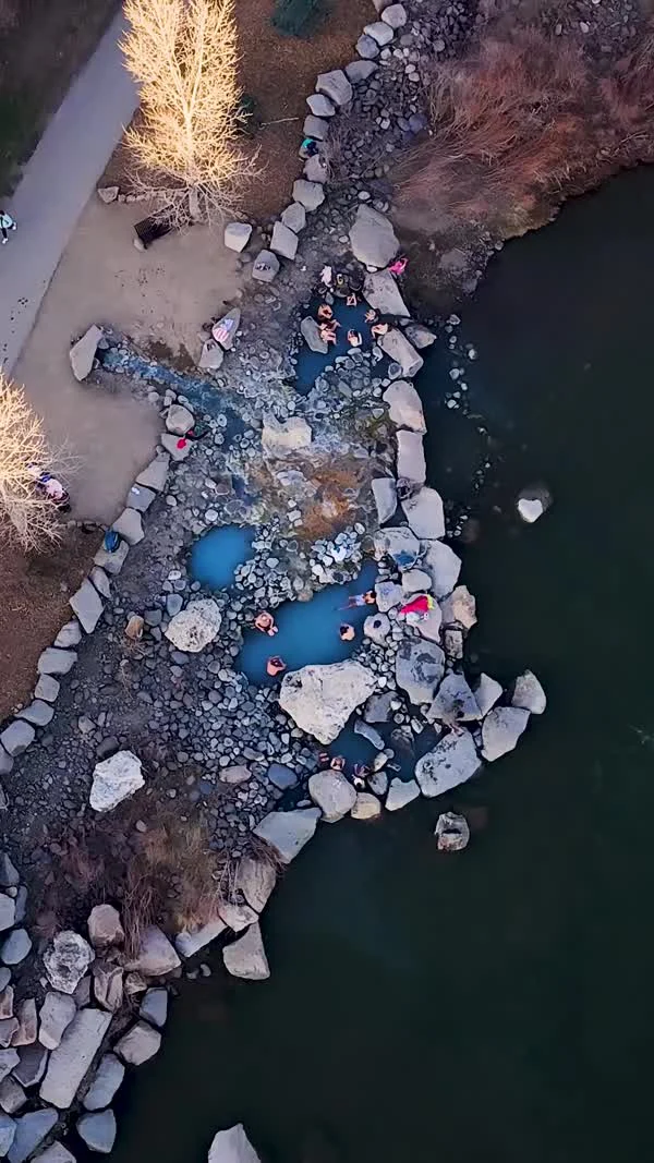 People sit in small rock-lined pools beside a river.