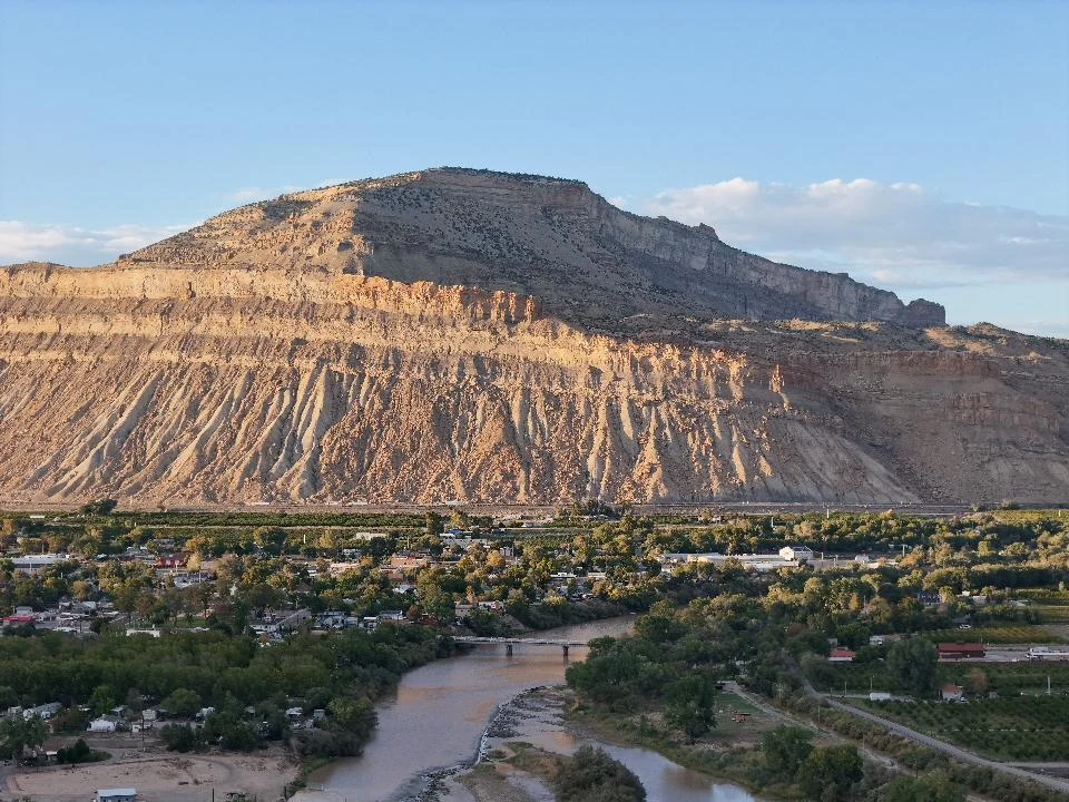 River bend, homes and cultivated rows beneath layered cliffs near Palisade