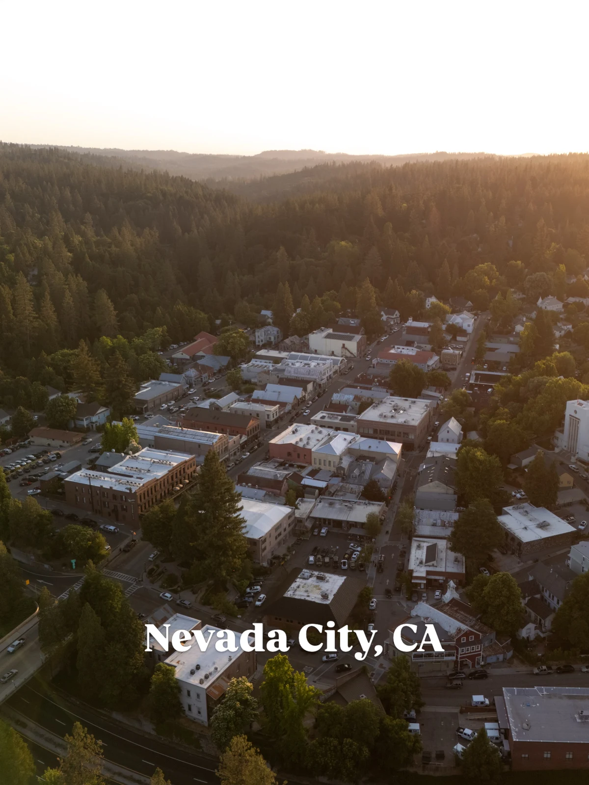 Nevada City rooftops among forested foothills at sunset