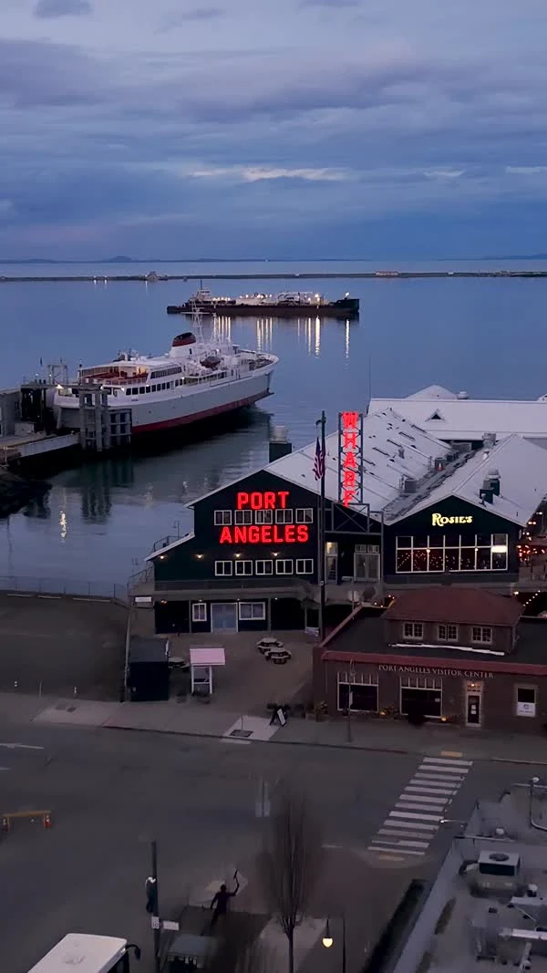 A ferry sits on calm water behind a building with a red Port Angeles sign.