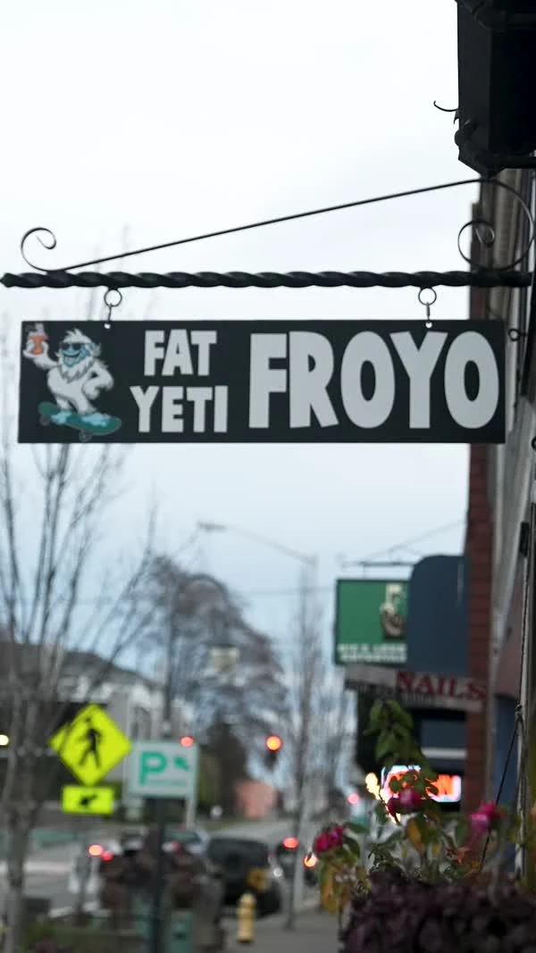 A Fat Yeti Froyo sign hangs above a downtown sidewalk.