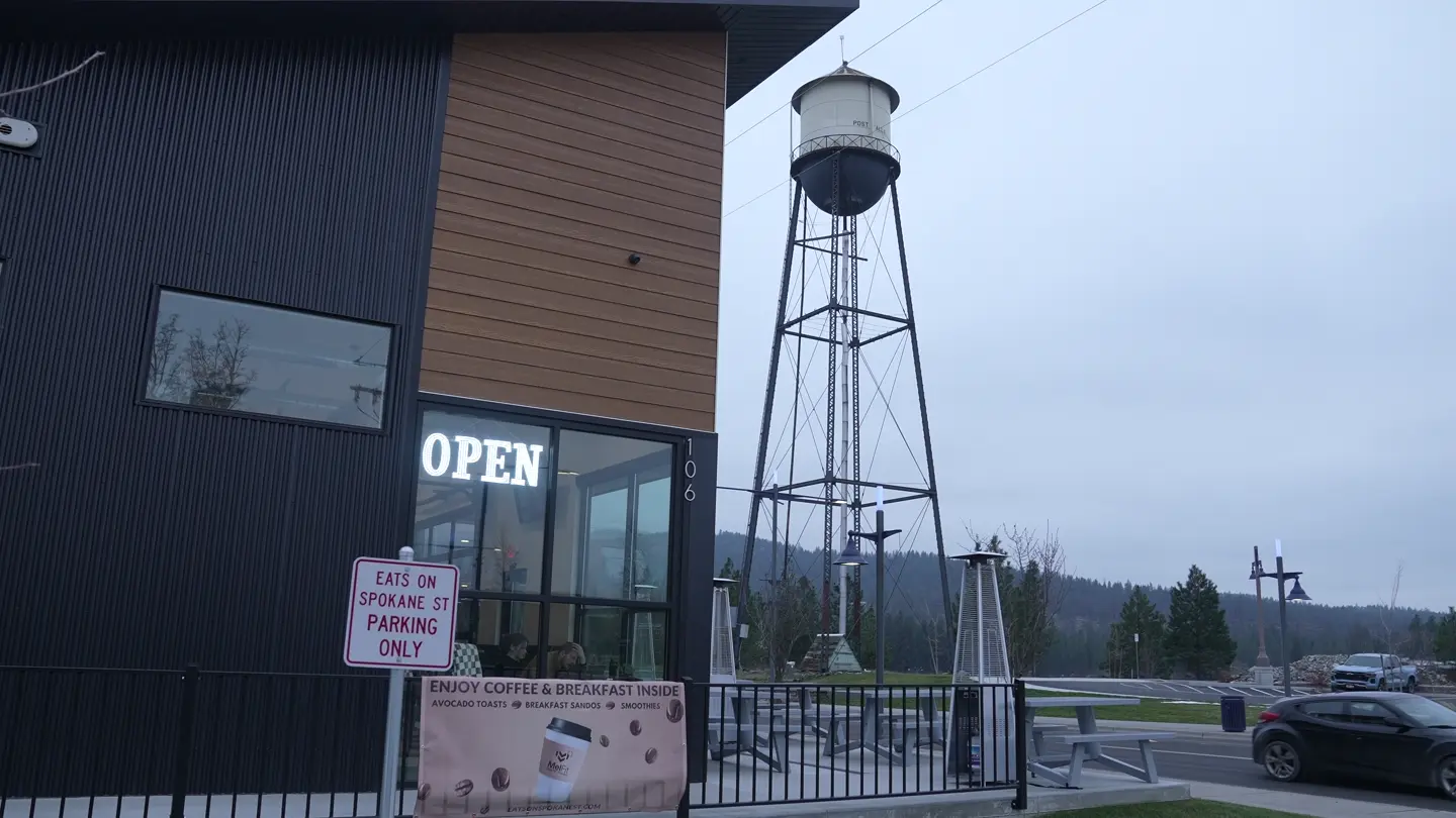 Open coffee storefront, parking signs and water tower behind it. Continuous single camera shot; no visible interview.