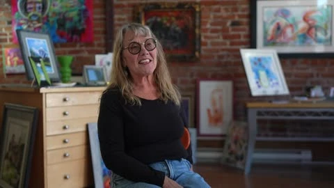 A participant sits among framed artworks inside a gallery.