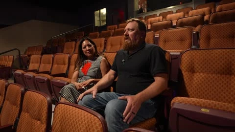 Two participants sit together among rows of theater seats.