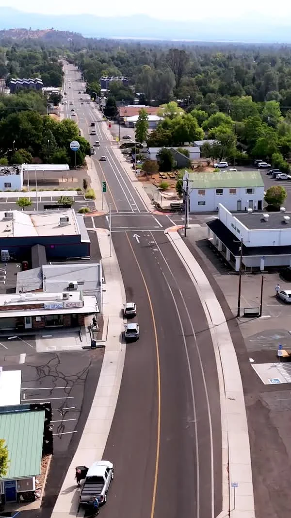An aerial view follows a broad road past Shasta Lake storefronts and trees.