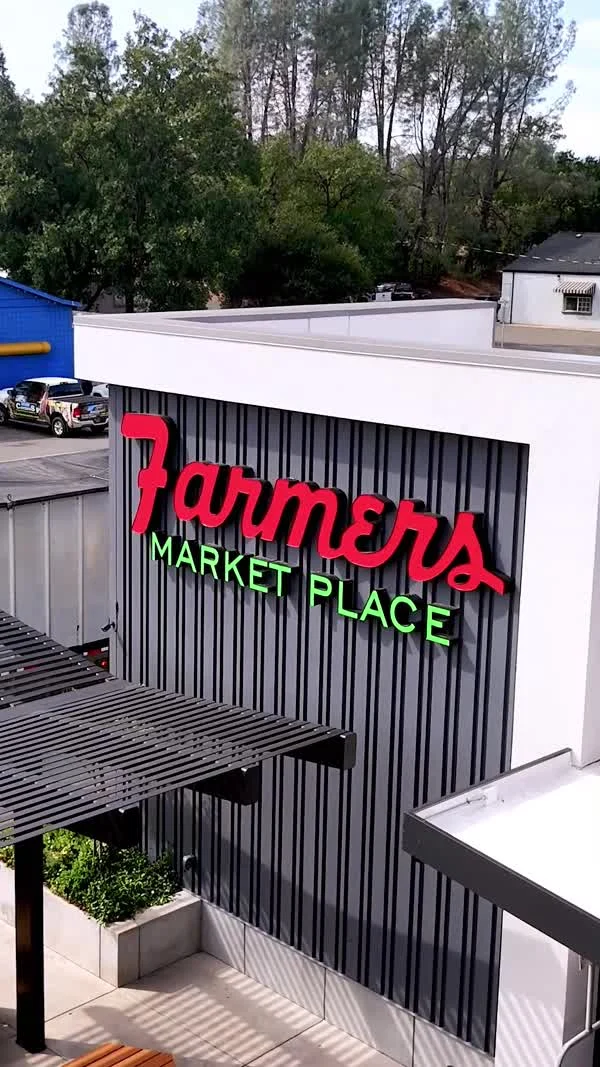 A red-and-green Farmers Market Place sign stands on a white building.