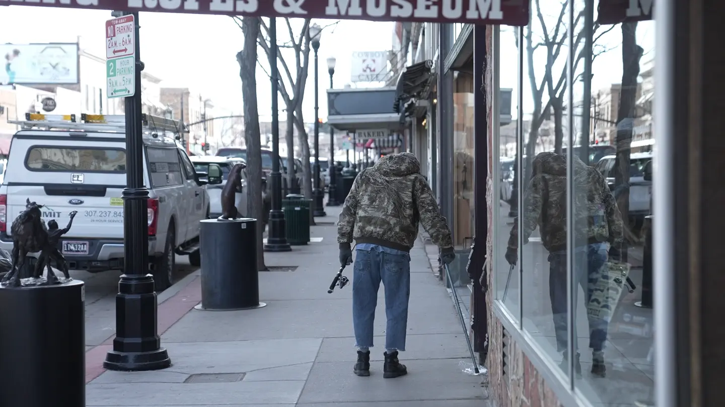 A person walks the sidewalk beneath a sign reading Ropes & Museum; storefronts, parked truck and public art appear. Person identity not asserted.