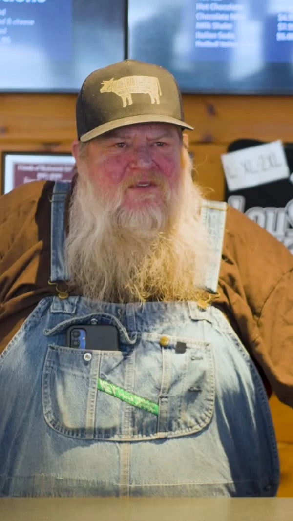 A bearded participant in overalls and a cap speaks inside a bar.