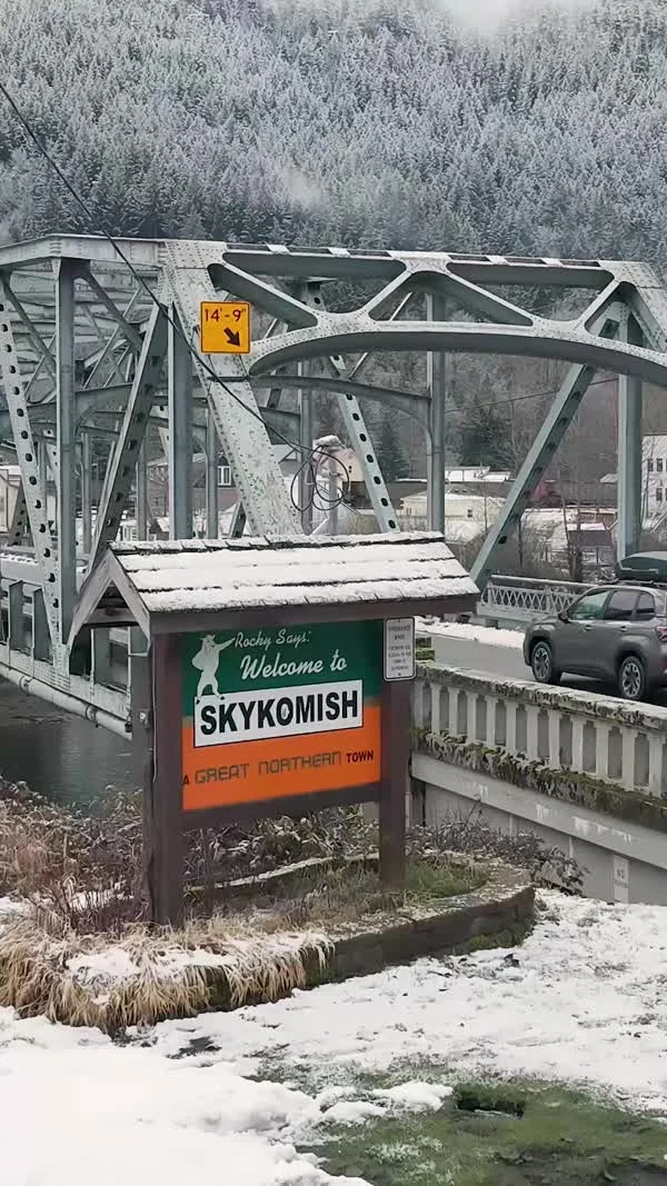 A steel bridge stands beside a sign welcoming visitors to Skykomish.