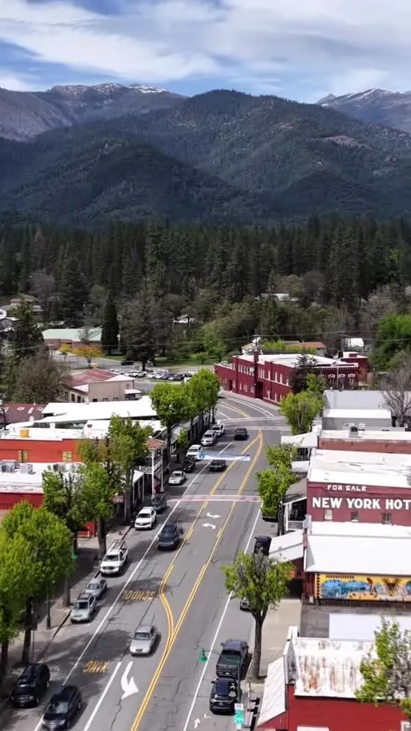 An aerial view follows Weaverville’s main street toward forested mountains.
